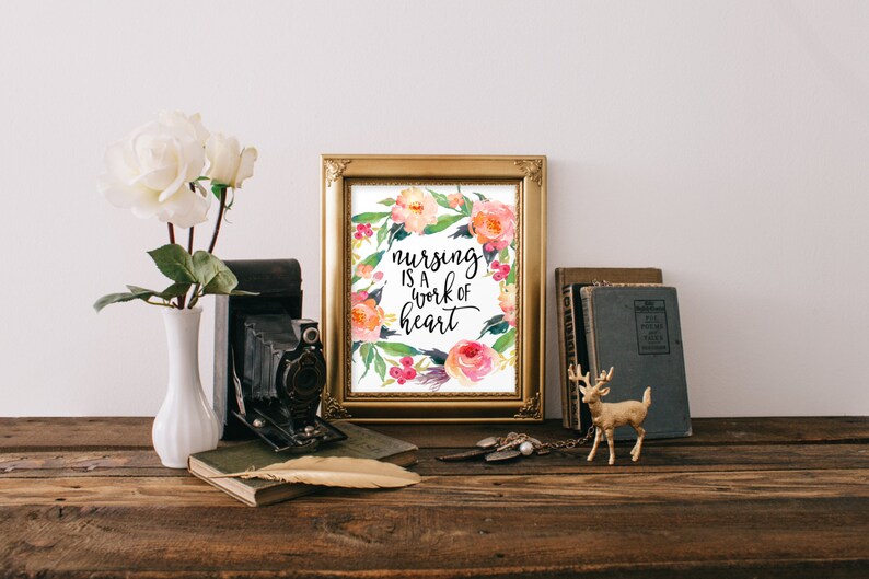 May include: A gold framed print with a watercolor floral wreath and the text "nursing is a work of heart".