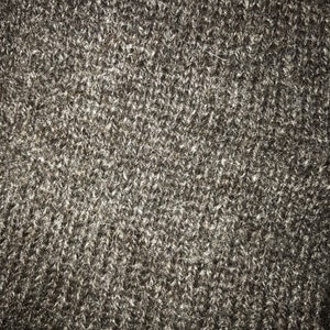 May include: Close-up of a dark gray knitted fabric with a fuzzy texture.
