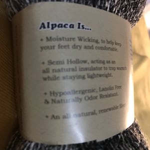 May include: Close-up of a brown label with the text "Alpaca Is..." and a list of benefits of alpaca fiber. The label is attached to a skein of black and white alpaca yarn.