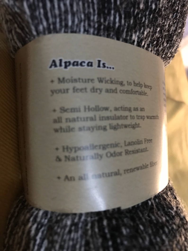 May include: Close-up of a brown label with the text "Alpaca Is..." and a list of benefits of alpaca fiber. The label is attached to a skein of black and white alpaca yarn.