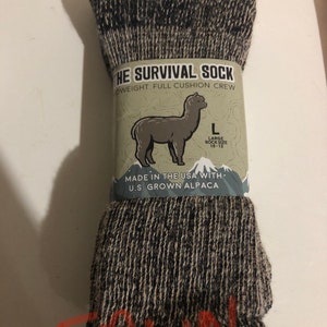May include: A pair of black and gray alpaca wool socks with a full cushion crew design. The socks are labeled "The Survival Sock" and are made in the USA with U.S. grown alpaca. The label also states "Large Sock Size 10-13".