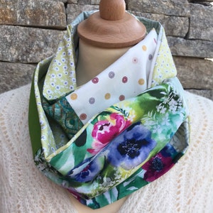 Peut inclure: Une écharpe infinie verte, blanche et bleue avec un imprimé floral. L'écharpe est en tissu et est pliée en boucle.