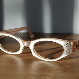 May include: White cat-eye glasses with a pink frame and rhinestones on the temples.