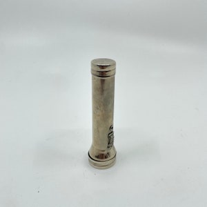 May include: A vintage silver flashlight with a cylindrical body and a textured finish. The flashlight has a round head and a base, with a small switch and emblem detail. The overall design is simple and functional.
