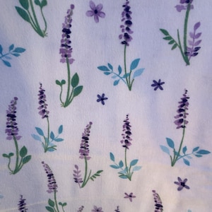 May include: White fabric with a repeating pattern of lavender sprigs and small purple flowers. The lavender is a deep purple color with green leaves and stems. The flowers are a lighter shade of purple, and the leaves are a mix of green and blue.