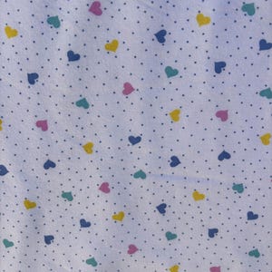 May include: White fabric with a repeating pattern of small, colorful hearts in blue, yellow, pink, and teal, interspersed with tiny blue dots. The hearts are scattered across the surface, creating a playful and cheerful design.