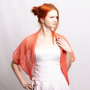 May include: A bright coral orange knit shrug with a loose, open-weave texture worn over a pale pink strapless bodice featuring a lace-trimmed neckline and a side-laced corset-style closure with matching ribbon ties.