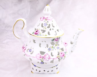 Può includere: Teiera in porcellana bianca con un delicato design traforato e accenti floreali. La teiera presenta fiocchi rosa, rose rosa e bianche e nontiscordardime blu. La teiera ha un bordo dorato e poggia su una base abbinata.