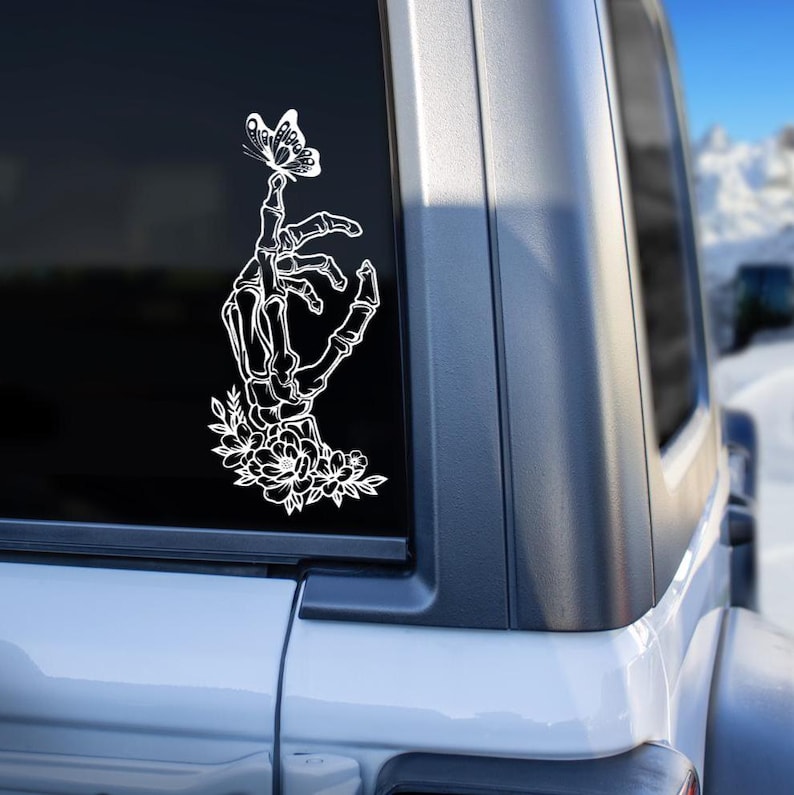 May include: A white skeleton hand with flowers and a butterfly on its finger. The hand is holding the butterfly gently.