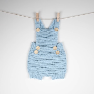 May include: A light blue crocheted baby overall with wooden buttons. The overall is hanging on a clothesline with wooden pegs.