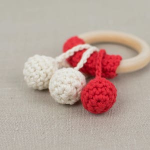 May include: A wooden teething ring with crocheted red and white pom-poms attached.