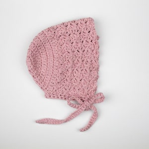 May include: A pink crocheted baby bonnet with a bow tie. The bonnet is made from soft, delicate yarn and has a classic design.