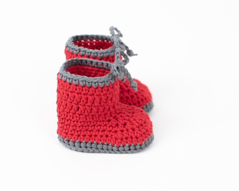 Op de afbeelding: Rode gehaakte babyschoentjes met grijze afwerking en strikjes.