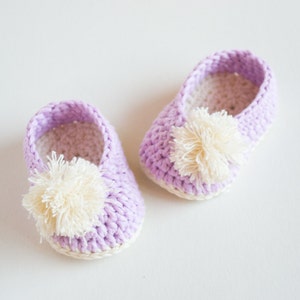 May include: A pair of lavender crocheted baby booties with white pom-poms.