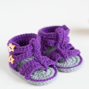 May include: Purple crocheted baby sandals with gray soles and wooden star buttons.