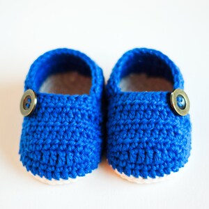 May include: A pair of blue crocheted baby booties with white trim and brown buttons.