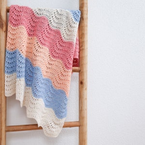 May include: A crocheted baby blanket with a wavy pattern in shades of pink, peach, blue, and white.
