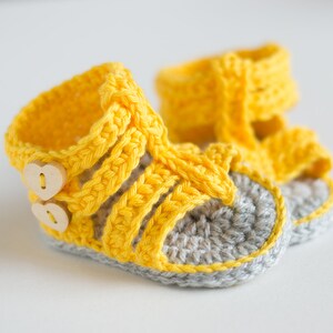 May include: A pair of yellow crocheted baby sandals with gray soles and wooden button accents.