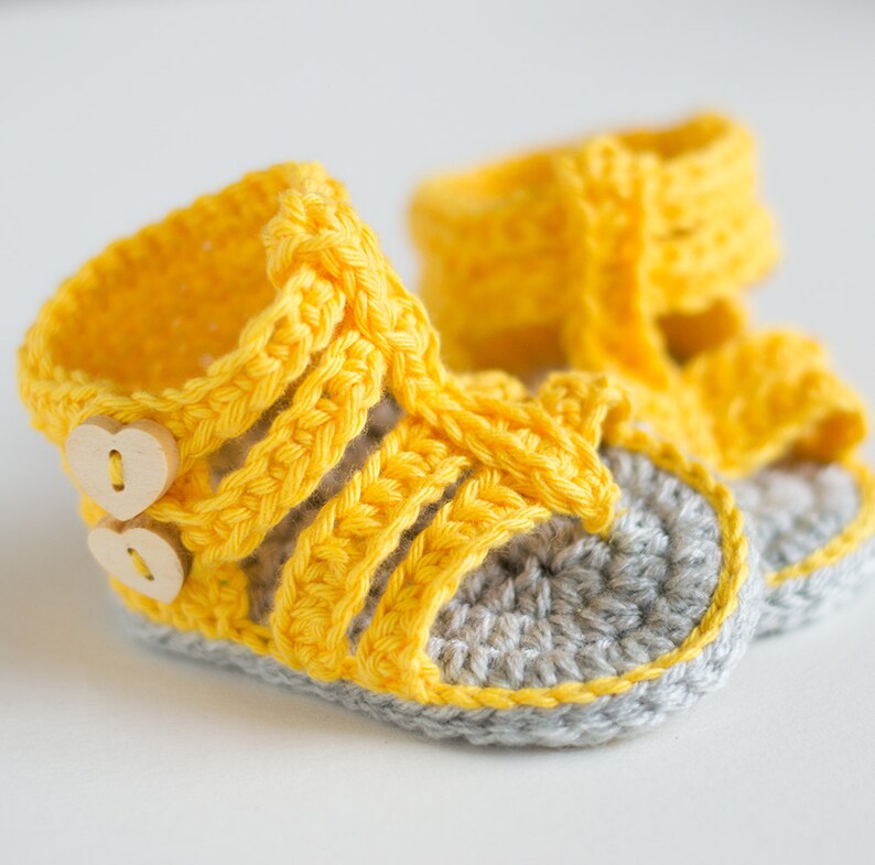 May include: A pair of yellow crocheted baby sandals with gray soles and wooden button accents.