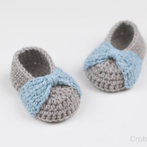 May include: A pair of grey and blue crocheted baby booties with a bow on the front.