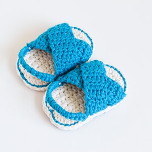 May include: A pair of crocheted sandals in white and blue. The sandals have a criss-cross strap design and are made with a soft, textured yarn.