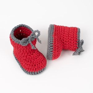 Op de afbeelding: Een paar rode gehaakte babyschoentjes met grijze afwerking. De schoentjes hebben een simpel ontwerp en zijn perfect voor een pasgeborene.