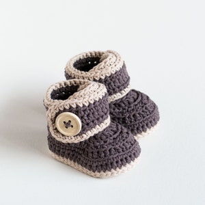 May include: A pair of crocheted baby booties in brown and beige with a wooden button on one bootie.