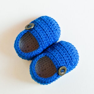 May include: A pair of blue crocheted baby booties with brown button accents.