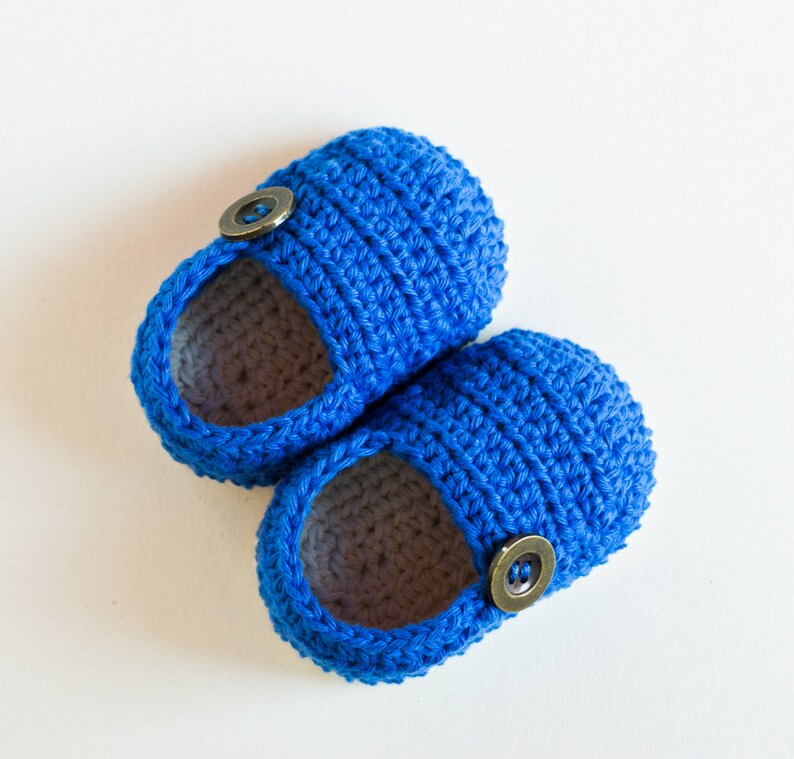 May include: A pair of blue crocheted baby booties with brown button accents.