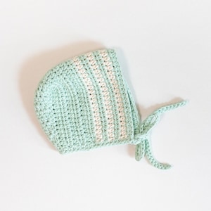 May include: A light green crocheted baby bonnet with white stripes and a tie.