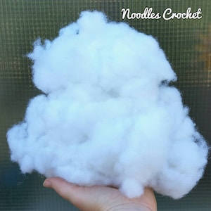 May include: A large quantity of white polyester stuffing, commonly used for filling plush toys and crafts. The stuffing is held in a hand, demonstrating its texture and volume.