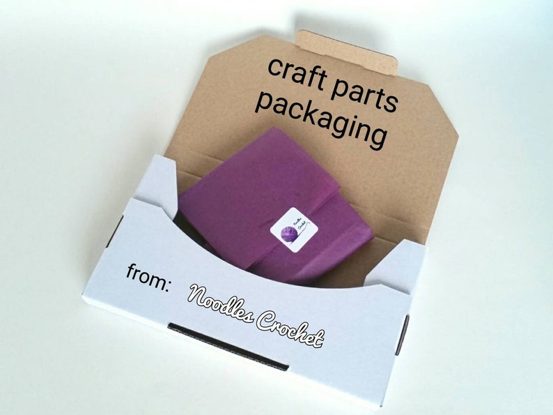 May include: A white box with the text "from: Noodles Crochet" on the bottom. The box is open and contains a purple tissue paper package with a small white sticker that says "Noodles Crochet". The box is labeled "craft parts packaging" on the top.