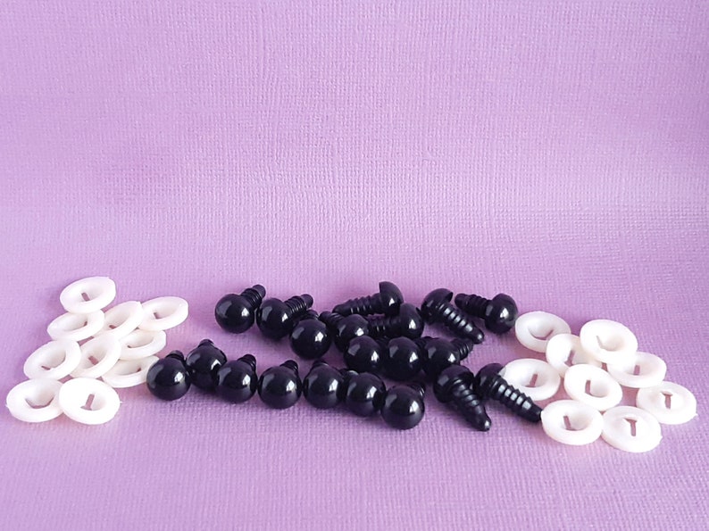 May include: A collection of black plastic safety eyes with screw backs and white plastic washers. The eyes are arranged in a pile on a purple surface.