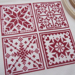 Può includere: Quattro motivi a punto croce rosso e bianco su uno sfondo di tessuto bianco. Ogni motivo è un design geometrico diverso.