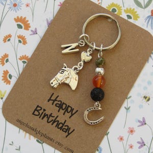 May include: A silver keyring with a horse head charm, the letter "N", and a horseshoe charm. The keyring also features a strand of colourful beads. The card reads "Happy Birthday" with the Etsy shop's URL.