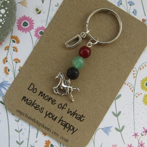 May include: A silver horse charm keyring with a silver letter D charm, red, green, and black lava beads, and a card that reads "Do more of what makes you happy".