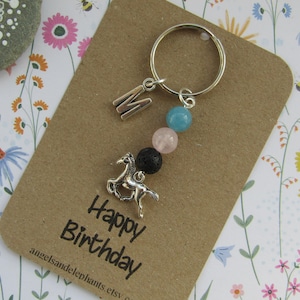 May include: A brown card with the text "Happy Birthday" and the words "angelsandelephants.etsy.com" printed on it. A silver charm with a horse design is attached to a silver key ring with a blue, pink, and black bead charm.