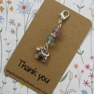 May include: A silver charm featuring a dog pendant, two gemstone beads, and a clasp. The charm is on a brown card with the words "Thank you" printed in black.