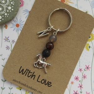 May include: A silver key chain with a horse charm, letter charm, and grey and brown beads. The keychain is on a brown card with the text "With Love" and "angelsandelephants.etsy.com".