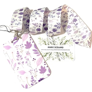 May include: A white lanyard and ID holder set with a floral pattern in shades of purple and lavender. The lanyard and ID holder feature a repeating design of leaves and flowers. A business card with the text "MARIE SCOLARO" is also visible.
