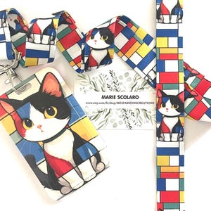 Peut inclure: Un cordon, un porte-badge et du tissu assorti sur le thème des chats. Le design présente un chat de dessin animé avec des accents noirs, blancs, rouges et bleus. Le cordon et le porte-badge ont un motif géométrique avec l'illustration du chat.