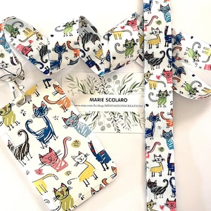 Peut inclure: Un cordon, un porte-badge et du tissu assorti blancs, ornés d'un motif de chats colorés. Les chats sont de différentes couleurs, dont le bleu, le rose, le jaune et le noir. Le porte-badge a une fenêtre transparente et un clip en métal.