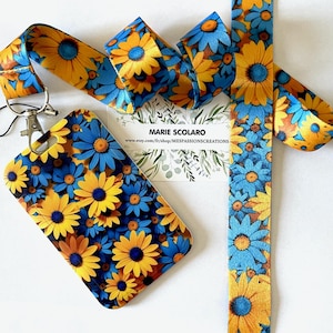 May include: A lanyard and matching cardholder featuring a vibrant floral pattern of yellow and blue daisies. The lanyard has a metal clasp and a matching daisy print. The cardholder is rectangular and also covered in the daisy design.