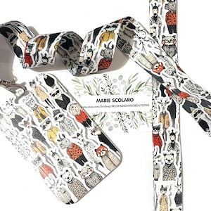 May include: A white lanyard, badge holder, and matching strap featuring a repeating pattern of anthropomorphic animals in various outfits. The lanyard has a metal clasp. A business card with the text "MARIE SCOLARO" is also visible.