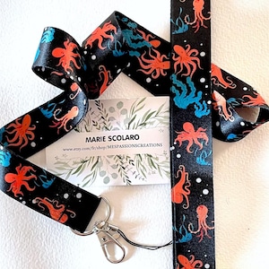 Puede incluir: Lanyard negro y blanco con un patrón repetido de ilustraciones de pulpos naranja y azul. El lanyard tiene un llavero plateado y un cordón negro. El texto "MARIE SCOLARO" y "www.etsy.com/fr/shop/MESPASSIONSCREATIONS" está impreso en una tarjeta blanca.