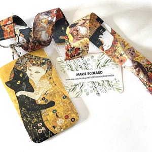 May include: A lanyard featuring a cat-themed design with a gold and black color scheme. The lanyard includes a card holder with a black and white cat illustration and the text "MARIE SCOLARO". The lanyard strap has a repeating pattern of cat portraits.