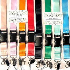 Peut inclure: Plusieurs lanières colorées, allant du rose à l'orange, en passant par le rouge, le noir, le vert et le bleu. Chaque lanière est équipée d'une boucle en plastique noir, d'un mousqueton métallique et d'une petite carte avec le texte "MARIE SCOLARO".