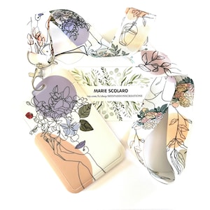 Puede incluir: Un cordón, un tarjetero y una tarjeta con motivos florales. El cordón y el tarjetero presentan un fondo blanco con dibujos lineales de flores y un rostro femenino. El tarjetero es de color blanquecino con una base color melocotón. La tarjeta tiene follaje verde.