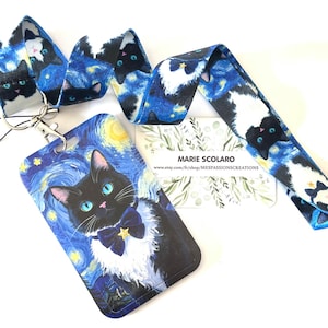 May include: A lanyard and ID holder set featuring a black cat design against a starry night background. The lanyard and ID holder have a blue and white color scheme. The ID holder has a black cat with a blue bow tie and a yellow star.