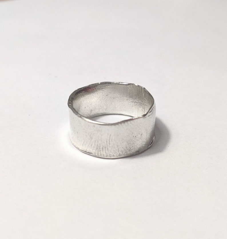 May include: A silver ring with a wide, textured band.